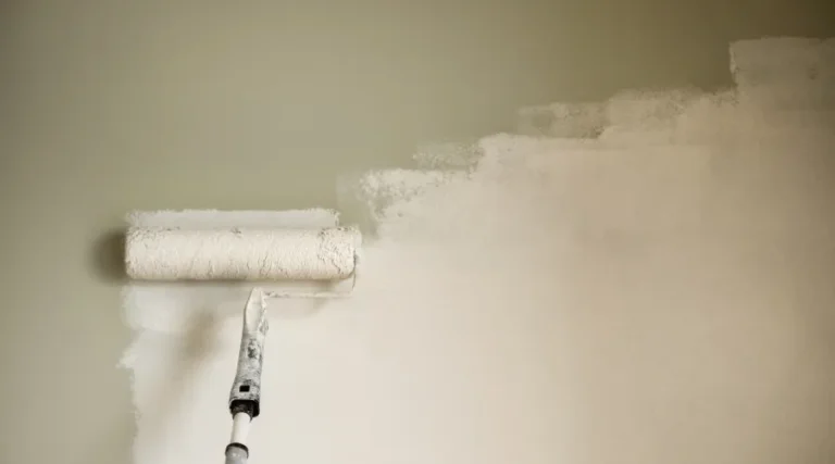 Paint roller applying white paint to a wall with a pale green background, showing a work-in-progress finish.