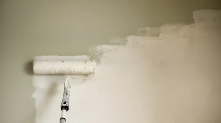 Paint roller applying white paint to a light wall, mid-stroke for a smooth coat.