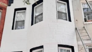 White-painted brick townhome facade with a curved bay and black window trim