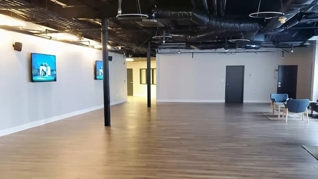 Open commercial office space with freshly painted gray walls, dark columns and ceiling, and wall-mounted screens